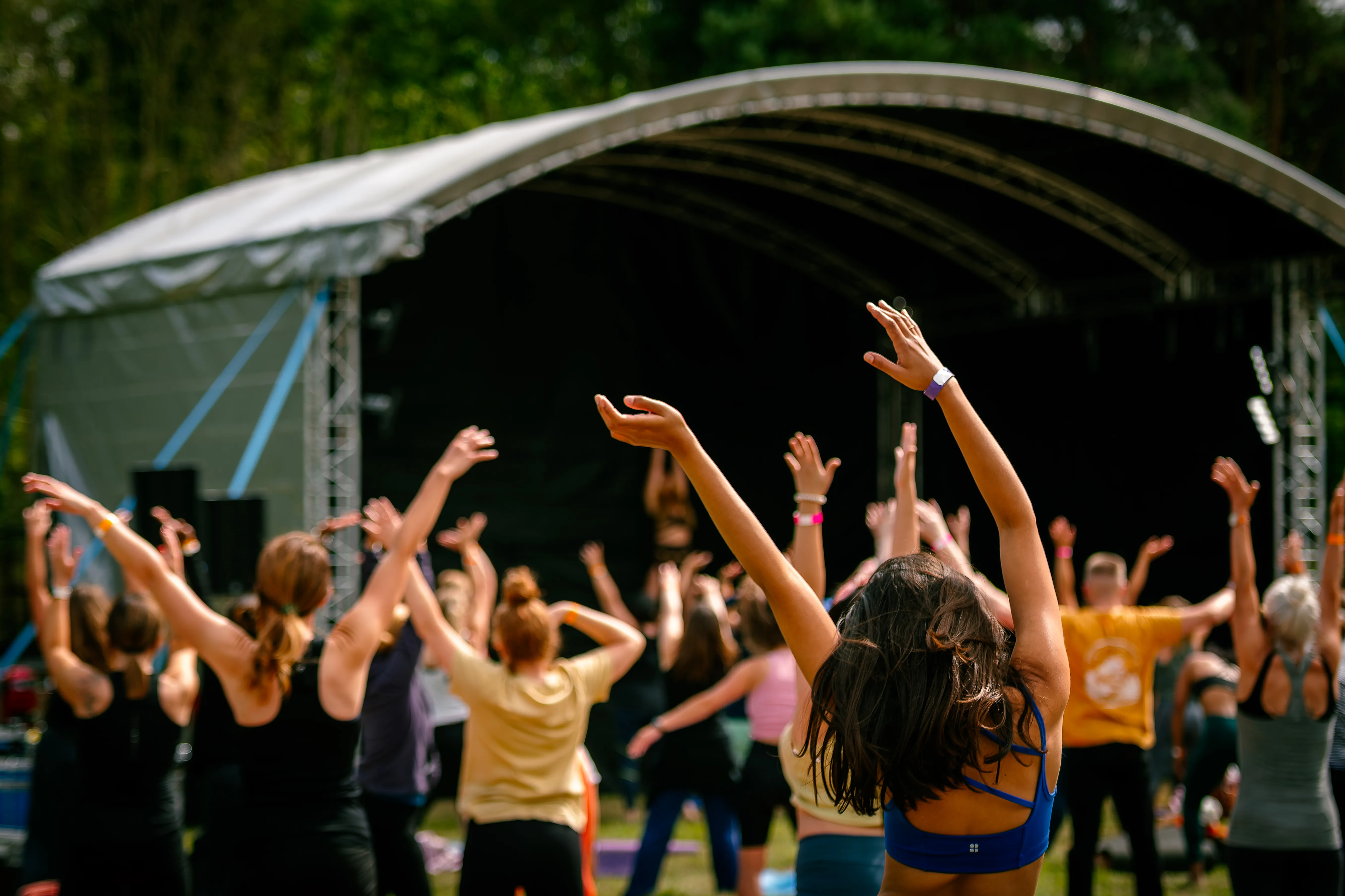 A field of people with their arms stretched skyward, moving together in front of the main stage.