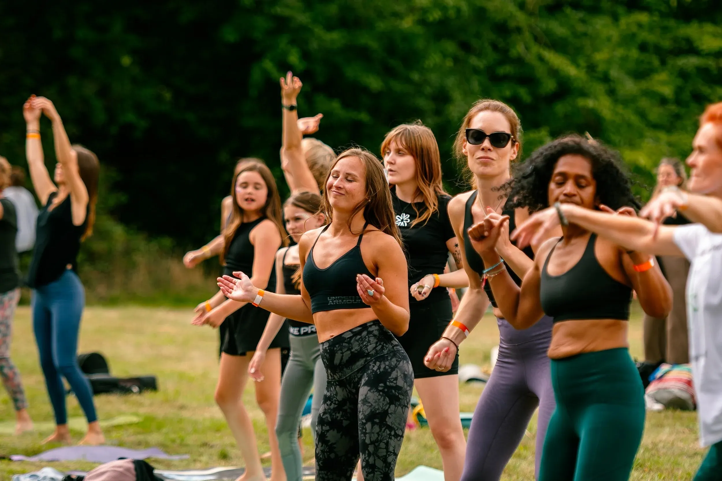 A group of women stretching and reaching upward together on the grass.
