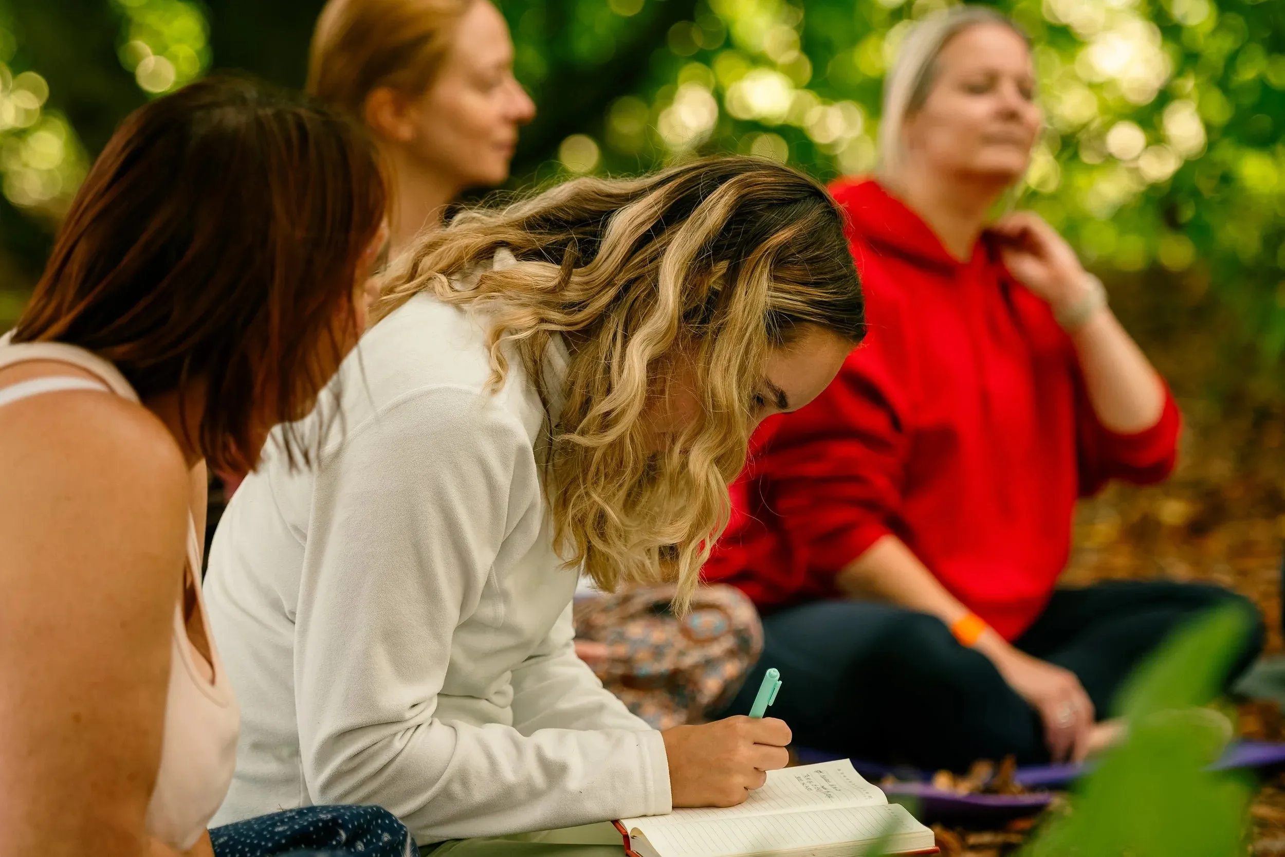 Women sitting together in soft light, one writing in a notebook during a workshop.