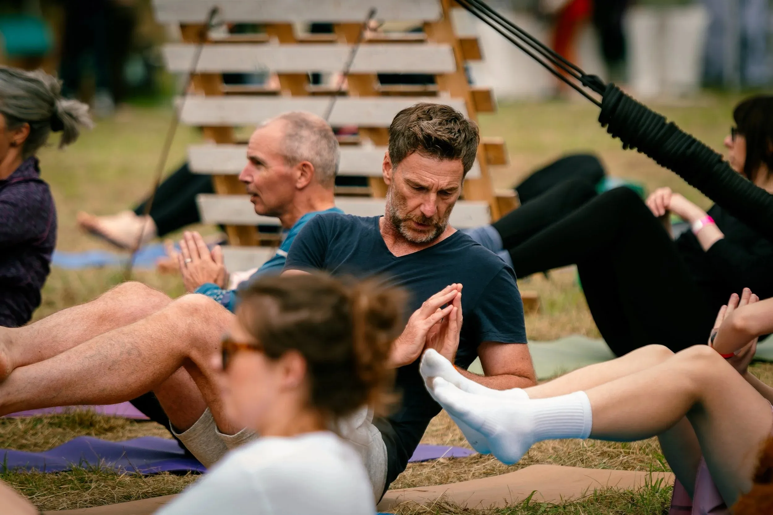 Pairs of people doing seated partner stretches on mats on the grass.