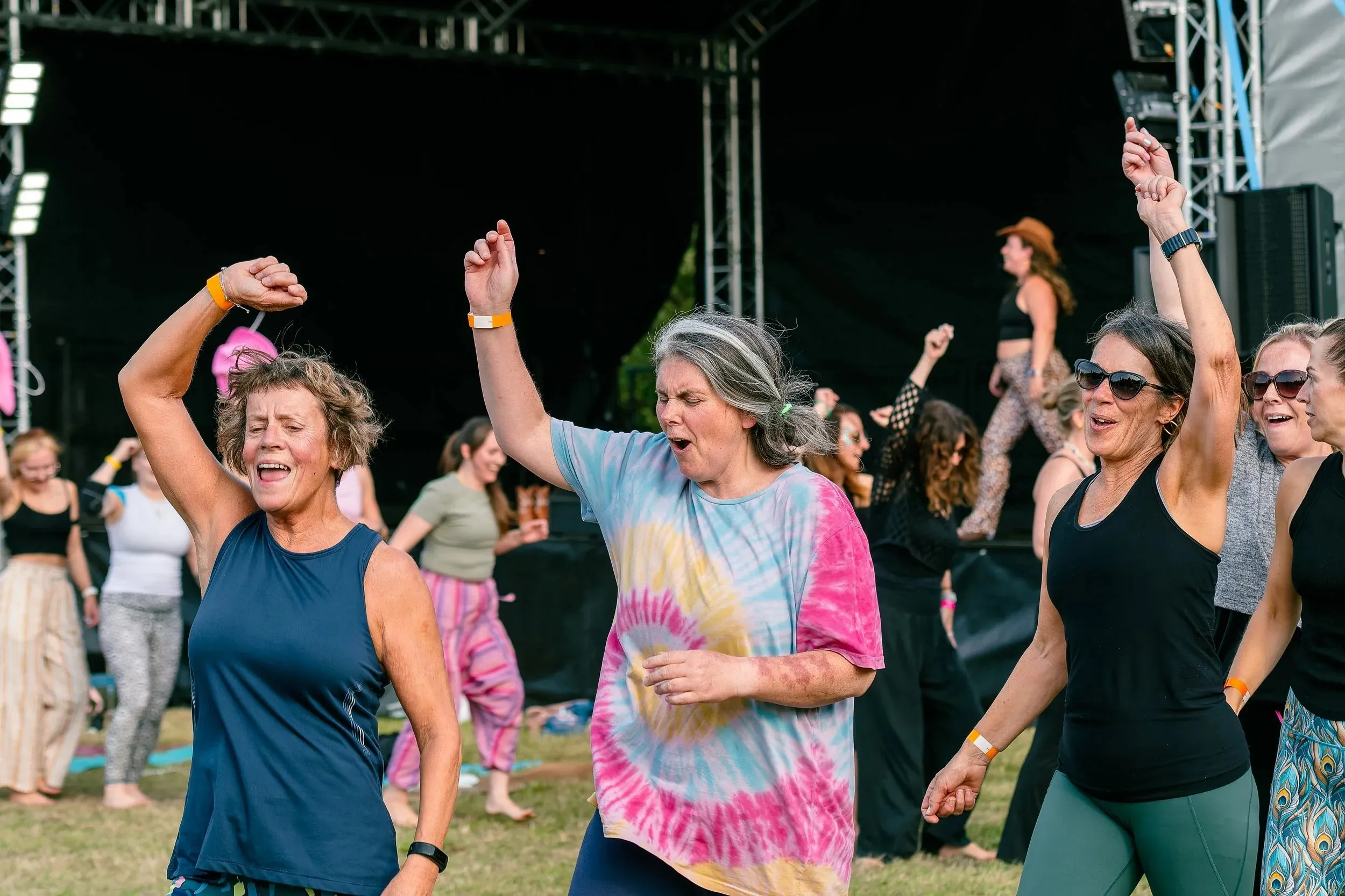 Women dancing near the stage, one in a tie-dye shirt, at the end of the day.