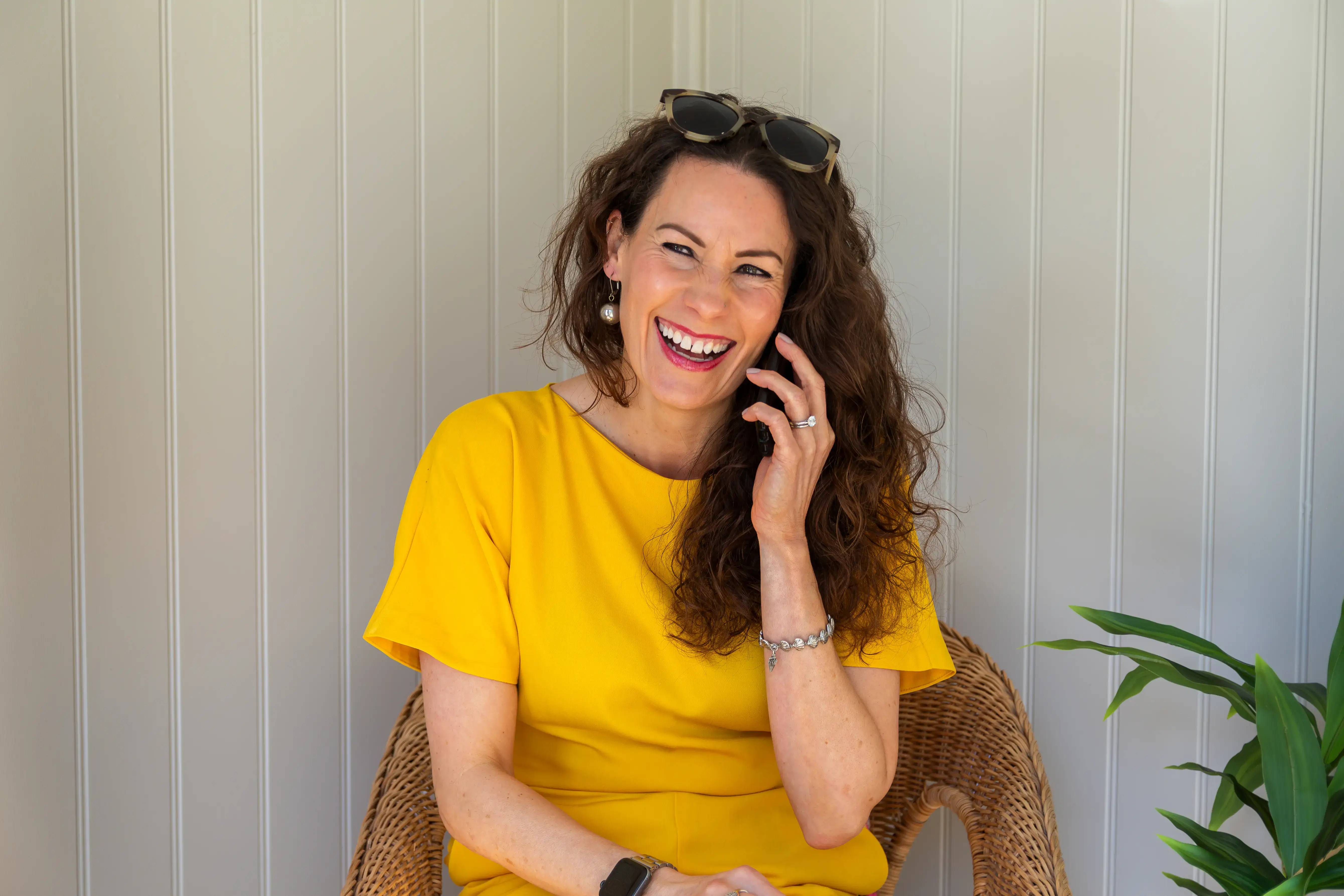 A female coach in a yellow dress laughing while on a client call