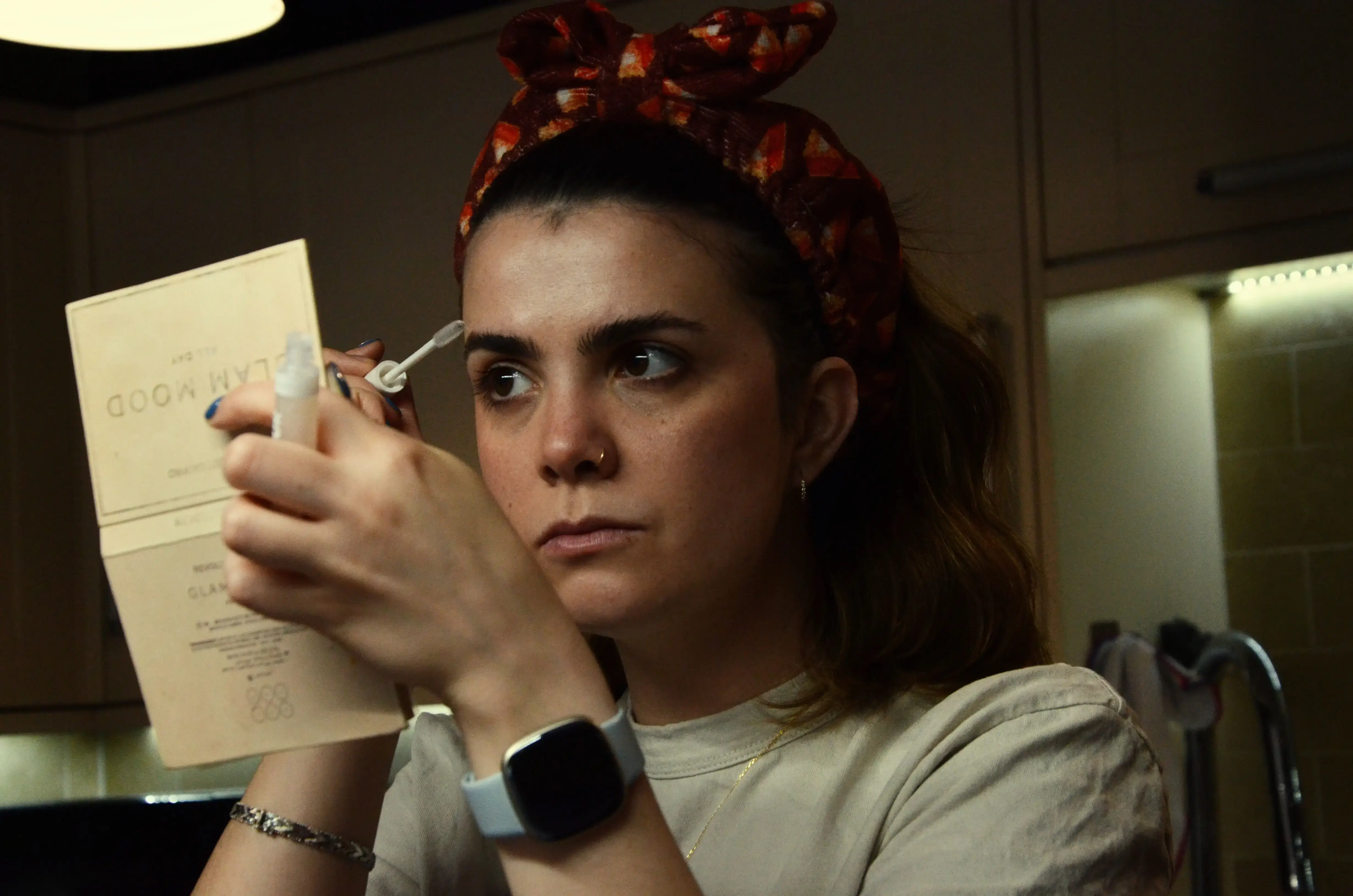 A young woman putting makeup on in her kitchen